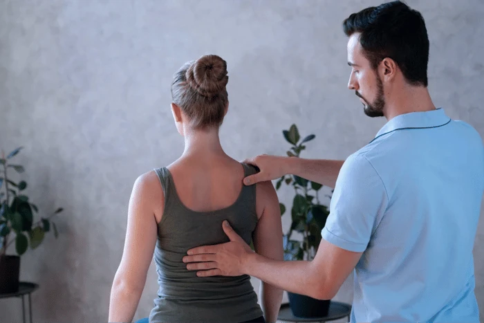 Chiropractor gently assessing a patient’s back and shoulder alignment while she stands